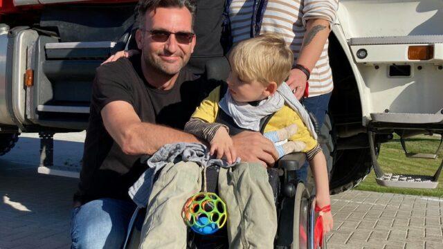 Eine Familie mit einem jungen im Rollstuhl steht vor einem Feuerwehrauto