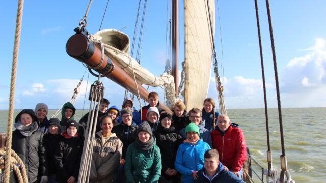 Eine Jugendgruppe steht bei windigem Wetter an Bord eines Segelschiffes auf dem Ijsselmeer.