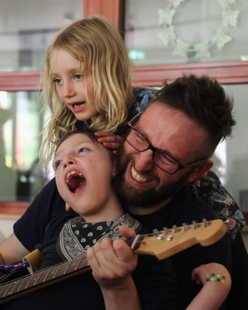 Ein Vater spielt im Kinderhospiz Löwenherz Gitarre mit seinen lachenden Kindern.