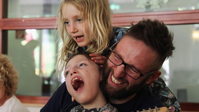 Ein Vater spielt im Kinderhospiz Löwenherz Gitarre mit seinen lachenden Kindern.