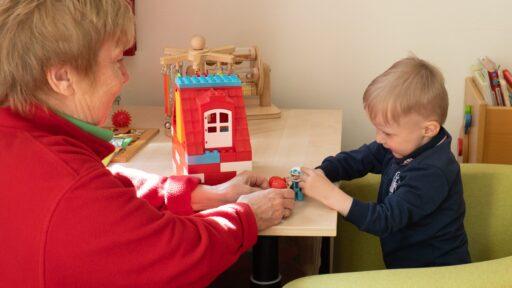 Eine ältere Frau spielt mit einem kleinen Jungen auf einem Tisch mit Duplo-Lego