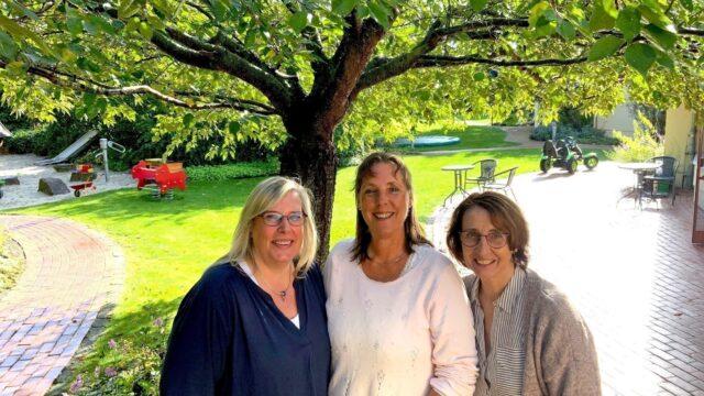Drei ältere Löwenherz-Pflegerinnen stehen unter einem Baum im Garten vom Kinderhospiz