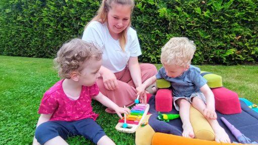 Eine junge Frau spielt mit zwei kleinen Kindern auf dem Rasen mit einen Xylophon.