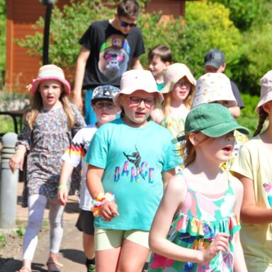 Ein Kinderchor marschiert in Zweierreihen singend durch den Löwenherz-Garten.