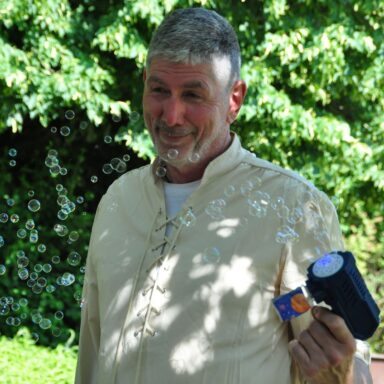Ein lachender Mann macht Seifenblasen mit einer Seifenblasenpistole.