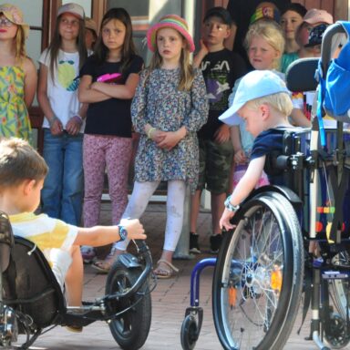 Ein kleiner Junge im Rollstuhl und ein Junge im Gokart hören einem Kinderchor zu.