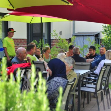 Eine Gruppe Menschen sitzt im Schatten unter Sonnenschirmen im Löwenherz-Garten