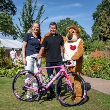 "Pastor Nowak" posiert im Löwenherz-Garten mit Löwenherz-Geschäftsführerin Kirsten Höfer, Maximilian Löwenherz und seinem Rennrad.