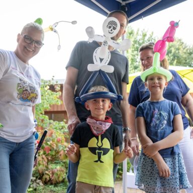 Zwei Kinder mit Luftballonfiguren als Kopfschmuck posieren mit ihren Eltern.