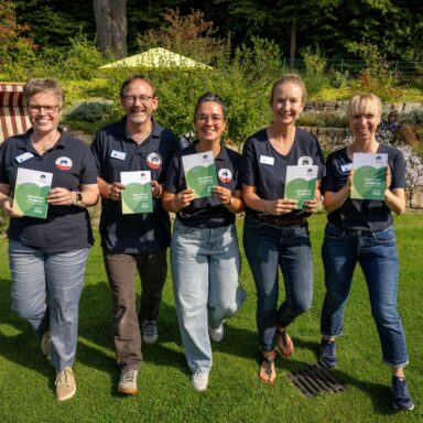 Fünf Menschen der Löwenherz-Akademie präsentieren das Programmheft 2026 im Löwenherz-Garten
