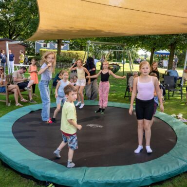 Kinder springen auf einem Trampolin im Löwenherz-Garten, im Hintergrund schauen Eltern zu