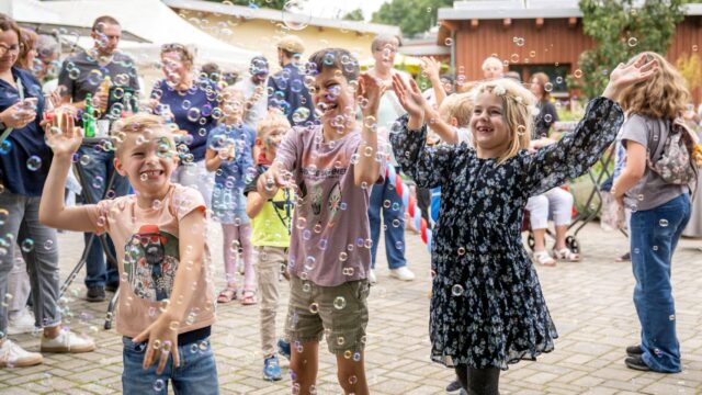 Drei Kinder stehen lachend in einem Meer von kleinen Seifenblasen.