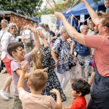 Eine Clownin macht zur Freude von Kindern viele kleine Seifenblasen.