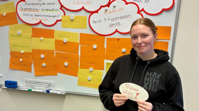 Ein junge Frau steht vor einem Whiteboard, an dem viele Karteikarten aus der Vorbereitung der Trainees hängen.