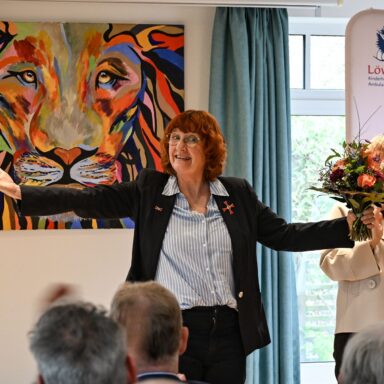 Gaby Letzing mit Bundesverdienstkreuz am Revers breitet die Arme aus und hält einen Blumenstrauß in der linken Hand.