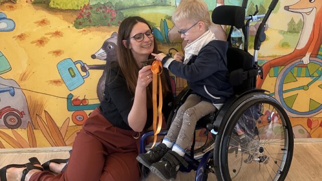 Juliane Schulze, Geschäftsführerin bei Löwenherz, übergibt zur Wiedereröffnung des Kinderhospiz Löwenherz symbolisch einen Schlüssel an einen kleinen, blonden Jungen im Rollstuhl.