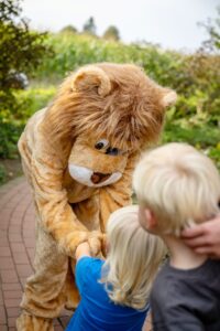 Zwei kleine Kinder mit blonden Haaren schütteln dem Löwenherz-Maskottchen die Hand